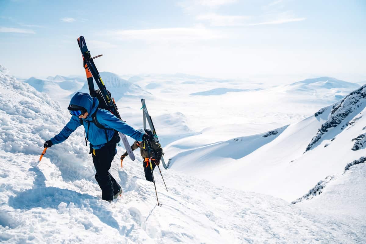 A ski tourer climbing a ridge with skis strapped to their pack, an open snow range opening up behind them.