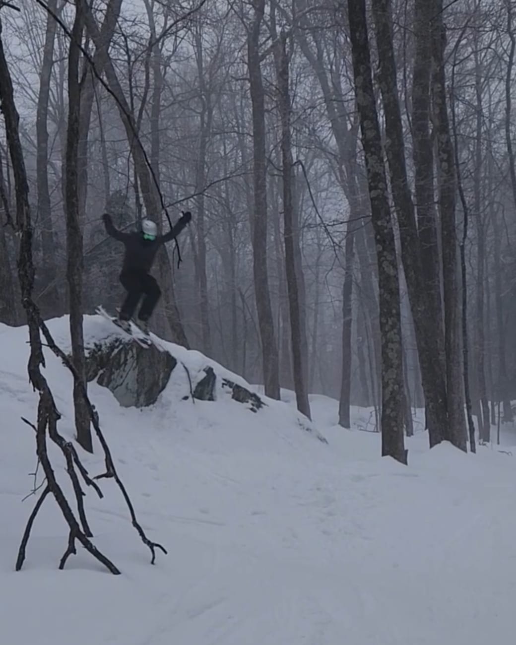 Jay skiing in the trees, in the air off a rock drop